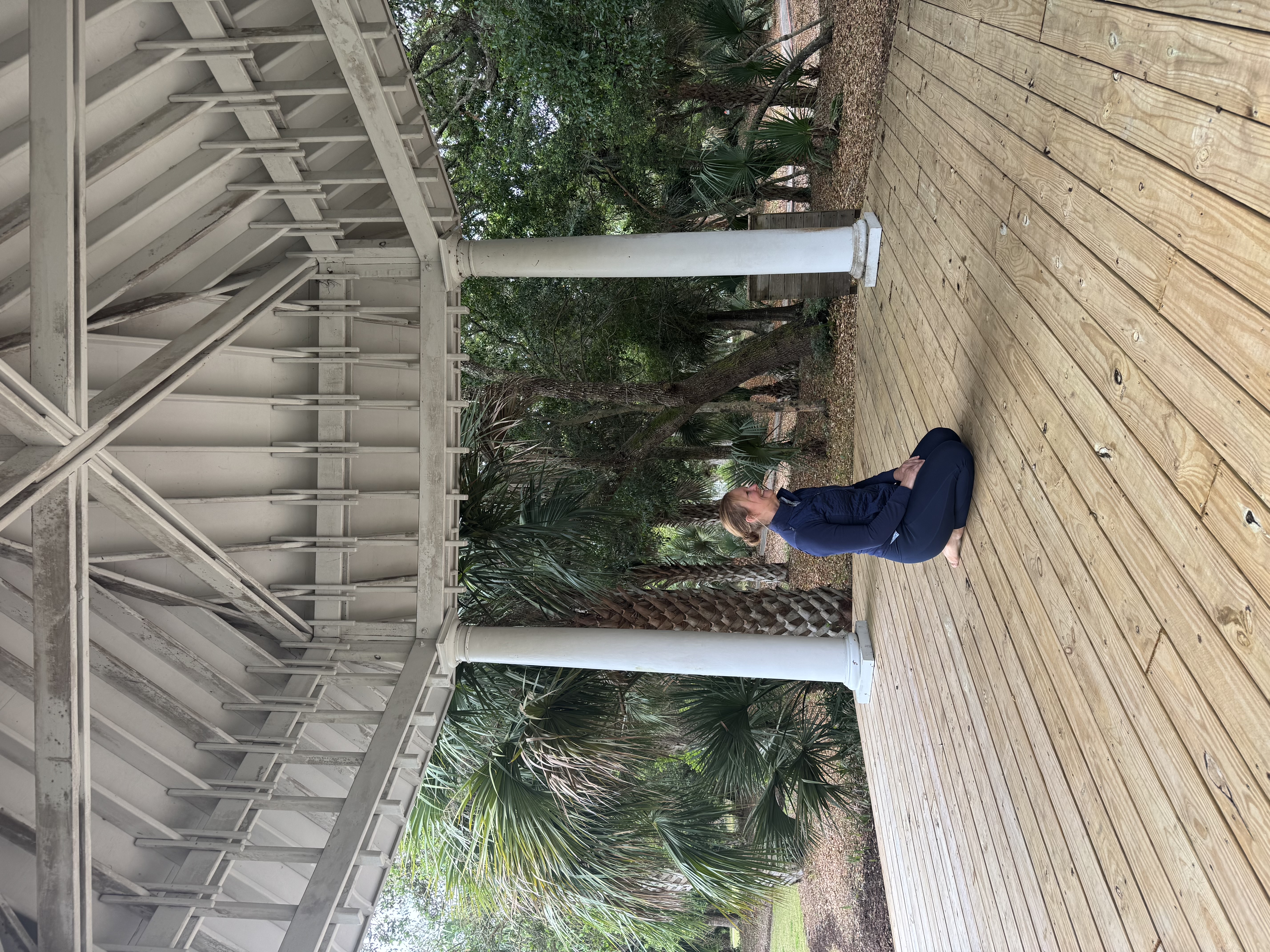 Woman in yoga pose on a wooden deck surrounded by palm trees